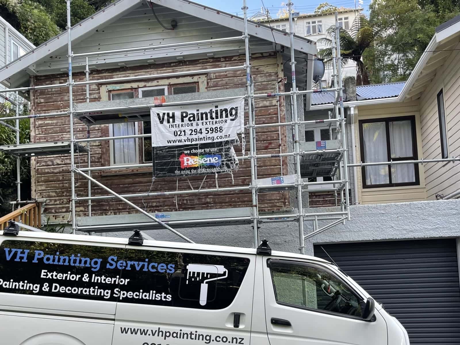 The bungalow before, with bare, weathered weatherboards behind the scaffolding